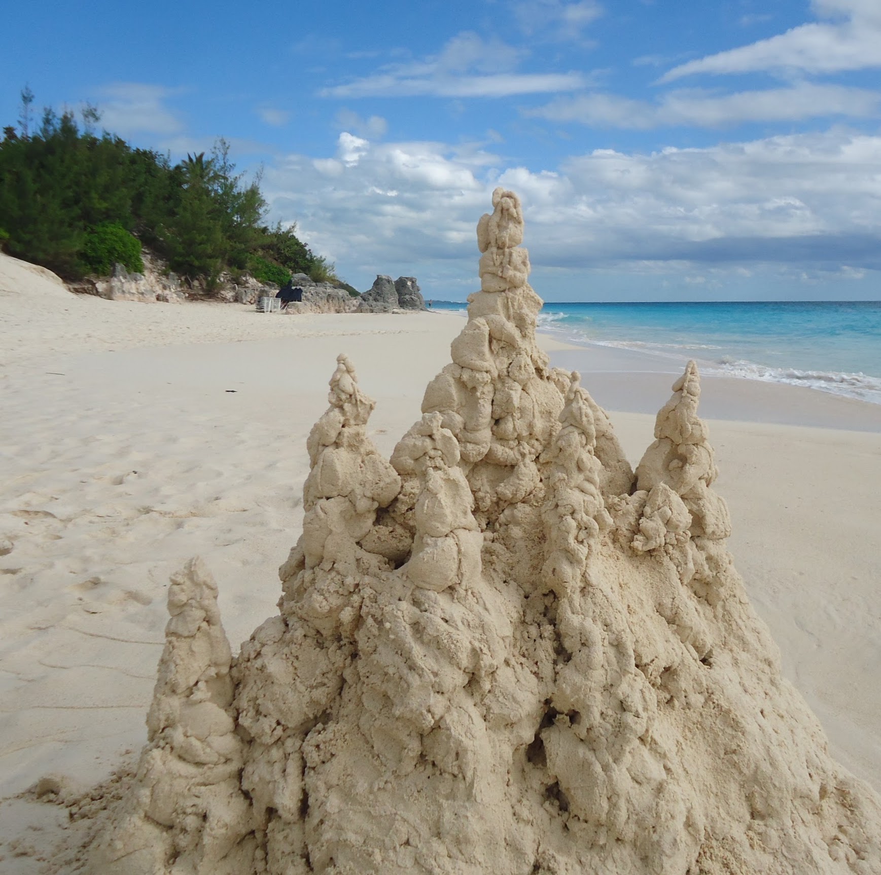 A tall drip sandcastle on a beach with no trench around it. The sand surrounding the castle is flat and undisturbed.